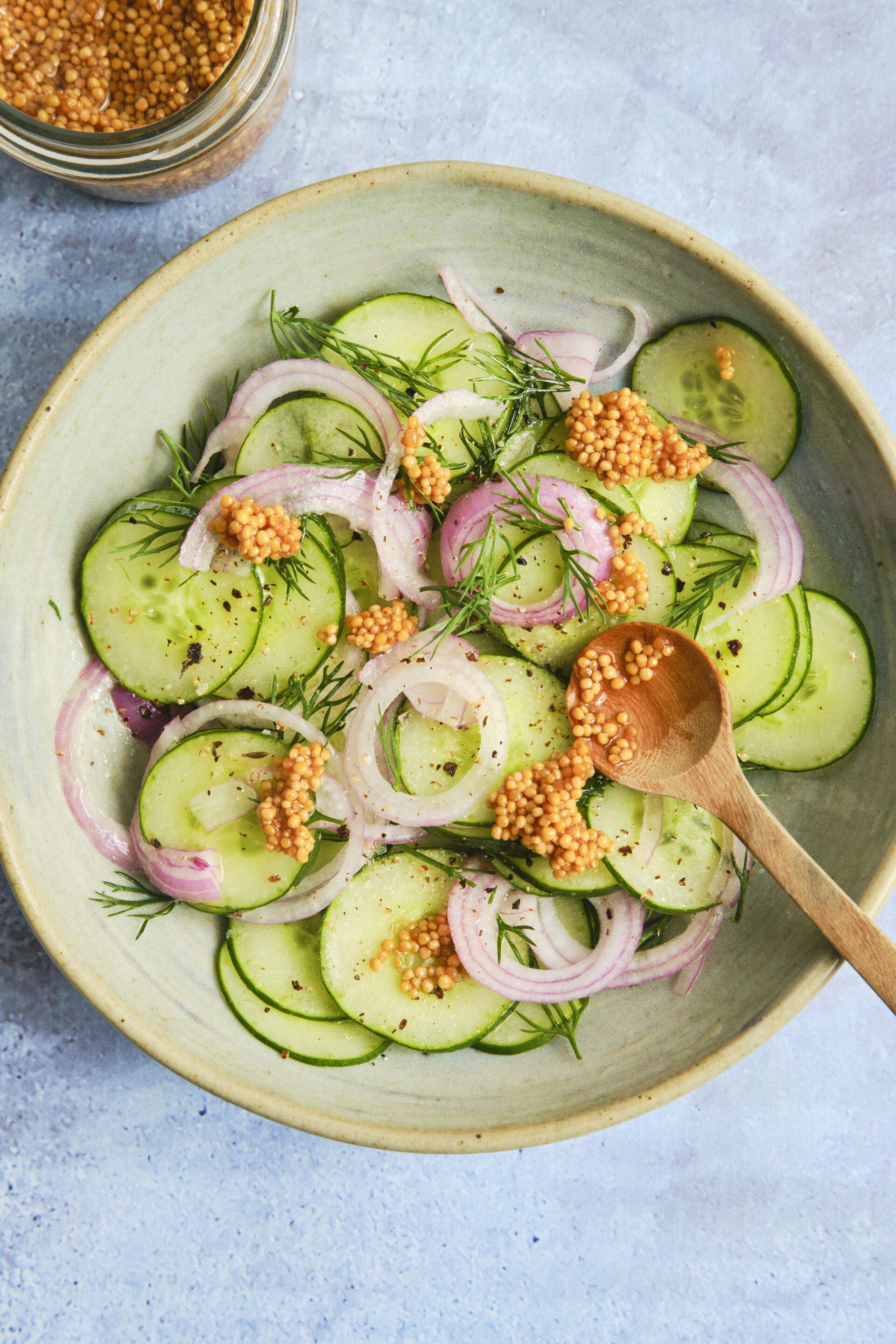 Fresh cucumber salad with thinly sliced red onions, garnished with pickled mustard seeds and chopped fresh dill in a light vinaigrette.