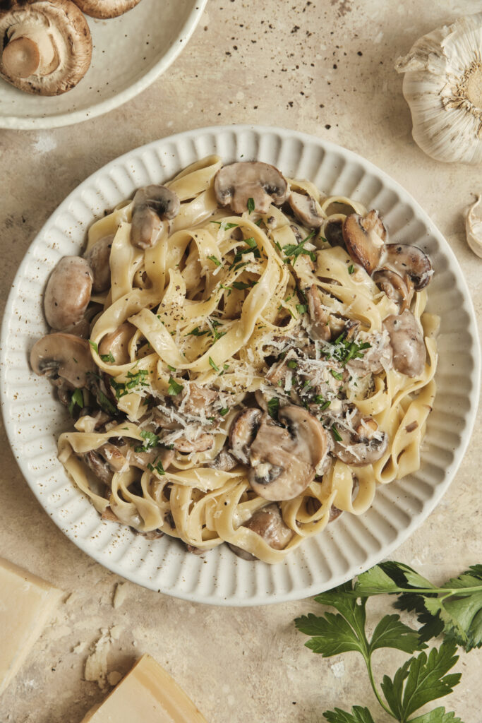 A bowl of creamy mushroom pasta with golden sautéed mushrooms, coated in a velvety cream sauce and topped with grated Parmesan and fresh parsley, served on a rustic plate.