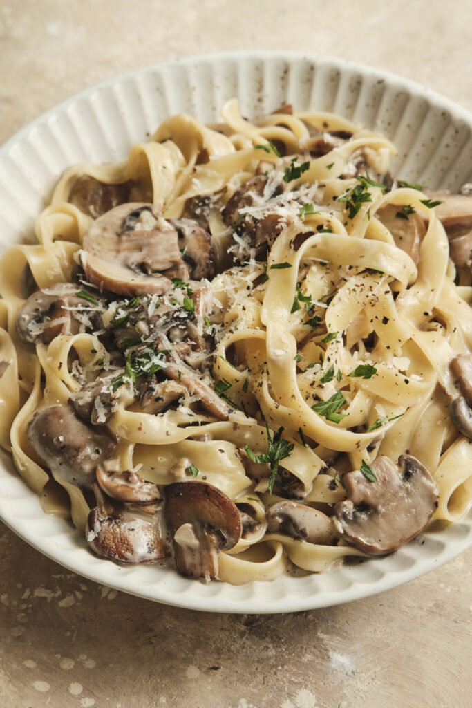 A bowl of creamy mushroom pasta with golden sautéed mushrooms, coated in a velvety cream sauce and topped with grated Parmesan and fresh parsley, served on a rustic plate.
