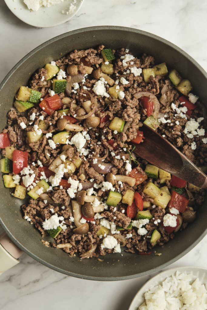 ground beef in a skillet with vegetables and feta cheese