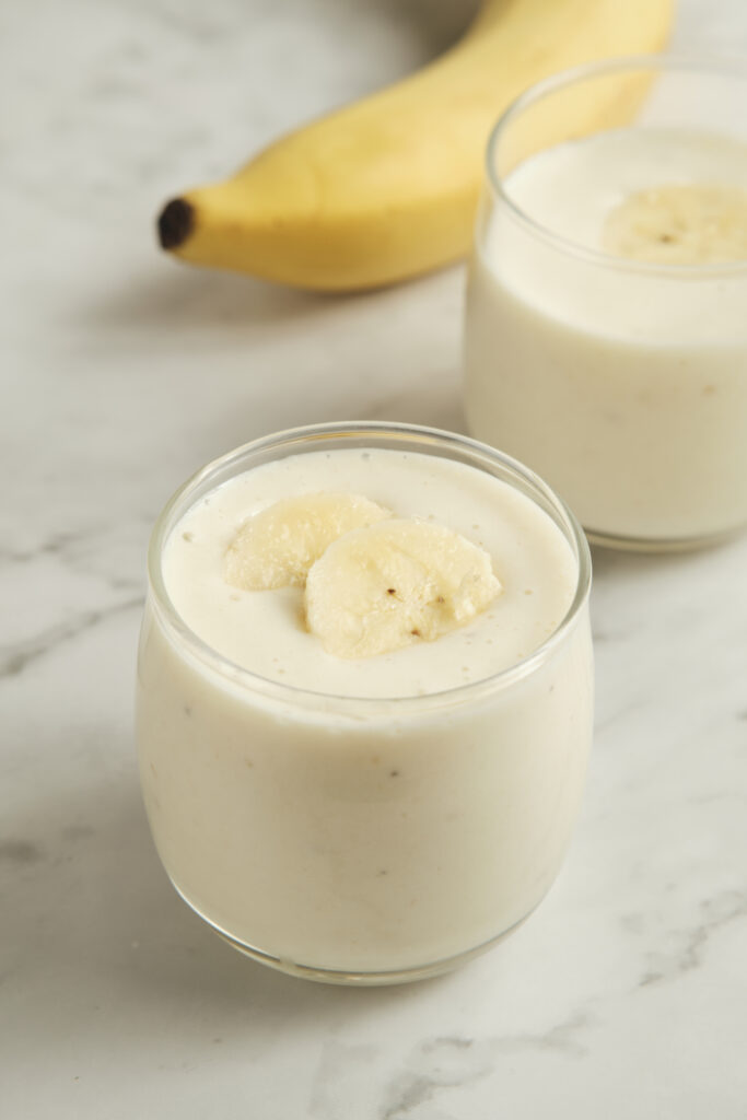 Creamy banana smoothie in a glass topped with sliced banana