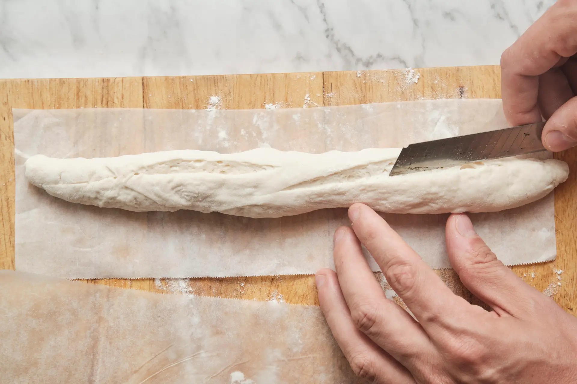 Shaped and proofed French baguettes being scored with a sharp knife before baking—step in a baguette recipe showing how to make baguette with proper scoring for oven spring and crisp crust.