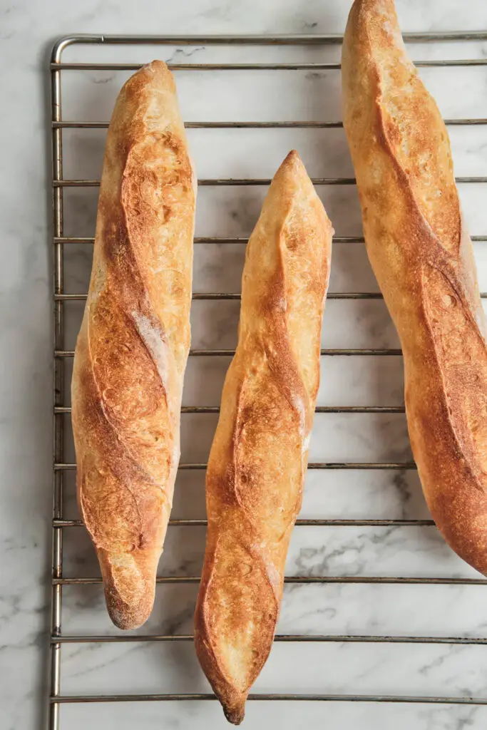 Golden brown freshly baked French baguettes straight from the oven with a crisp crust and airy interior—classic homemade baguette recipe results for how to make baguette.