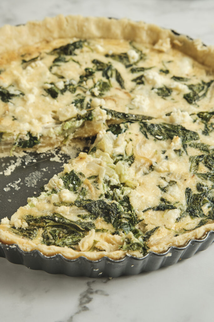 Baked spinach feta quiche with a golden crust and a sliced piece showing creamy filling—an easy spinach and feta quiche recipe perfect for vegetarian meals and simple quiche ideas.