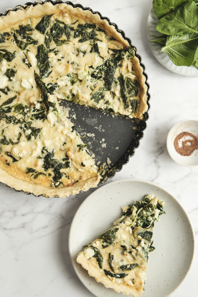 Baked spinach feta quiche with a golden crust and a sliced piece showing creamy filling—an easy spinach and feta quiche recipe perfect for vegetarian meals and simple quiche ideas.