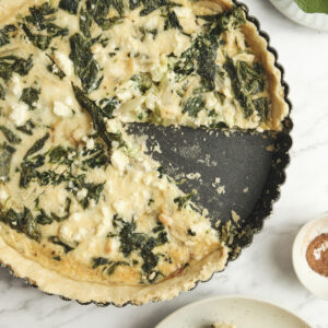 Baked spinach feta quiche with a golden crust and a sliced piece showing creamy filling—an easy spinach and feta quiche recipe perfect for vegetarian meals and simple quiche ideas.