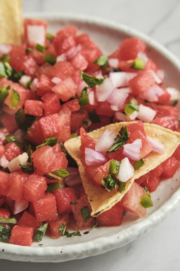 Watermelon salsa spooned over a nacho with fresh herbs and lime.