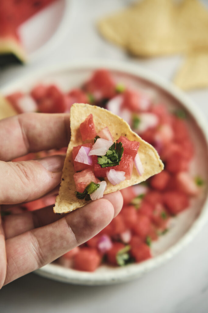 Watermelon salsa spooned over a nacho with fresh herbs and lime.