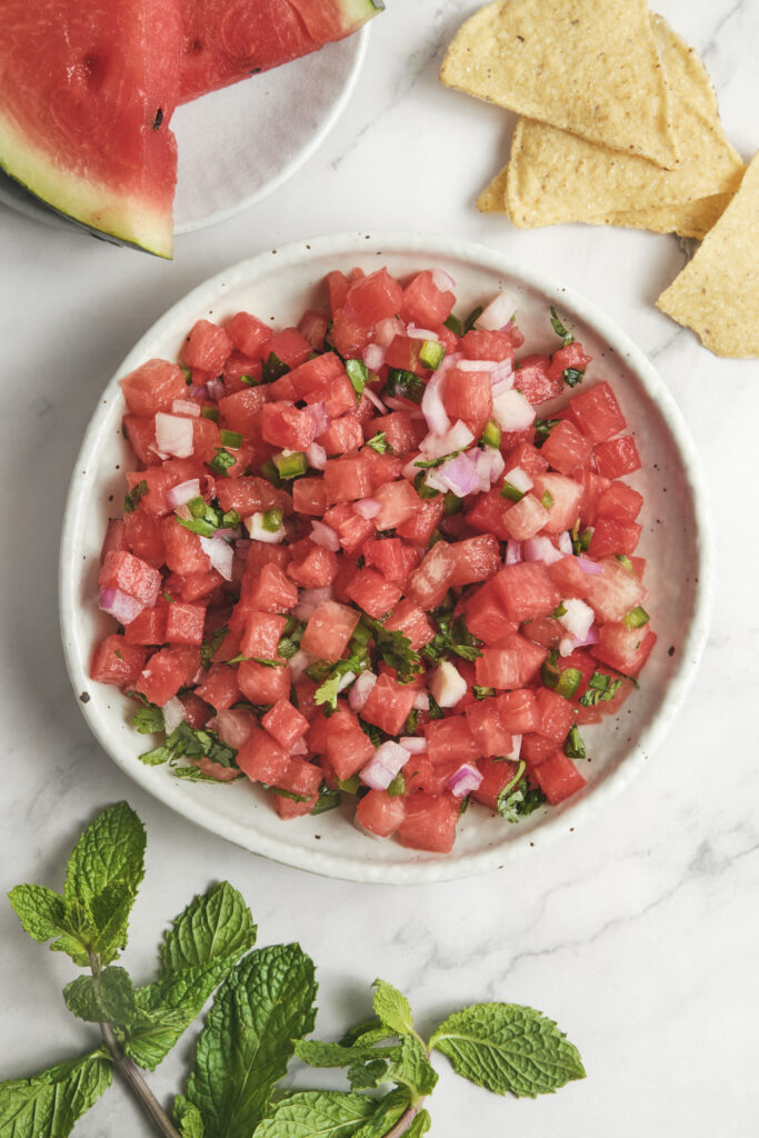 Fresh watermelon salsa served on a plate with lime, herbs, and jalapeño.