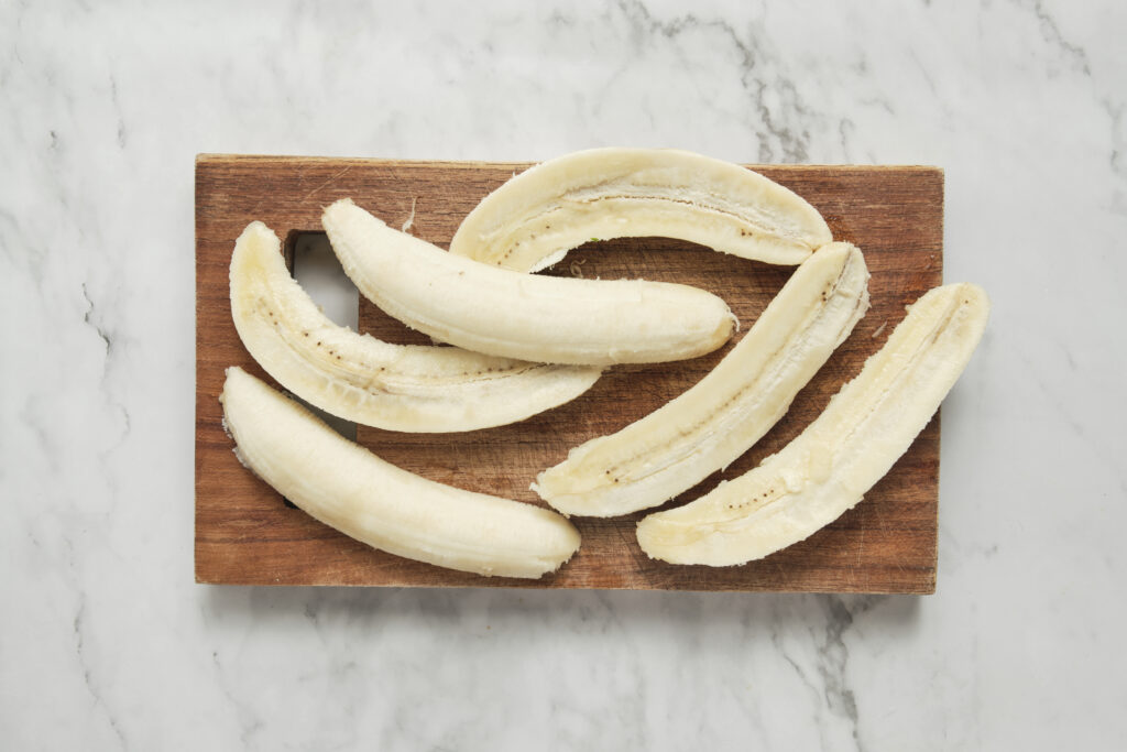 bananas being cut in half lenghtwise on a chopping board
