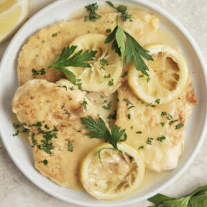 Chicken Francese served on a plate with golden pan-fried chicken breasts in a creamy lemon butter white wine sauce, garnished with fresh herbs and lemon slices.
