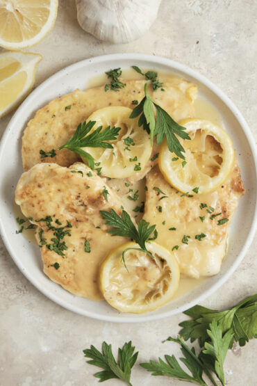 Chicken Francese served on a plate with golden pan-fried chicken breasts in a creamy lemon butter white wine sauce, garnished with fresh herbs and lemon slices.
