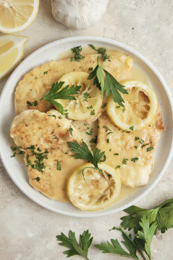 Chicken Francese served on a plate with golden pan-fried chicken breasts in a creamy lemon butter white wine sauce, garnished with fresh herbs and lemon slices.