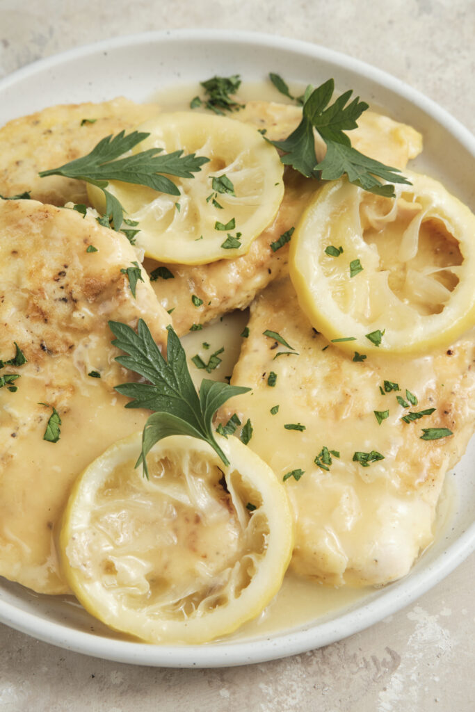Chicken Francese served on a plate with golden pan-fried chicken breasts in a creamy lemon butter white wine sauce, garnished with fresh herbs and lemon slices.