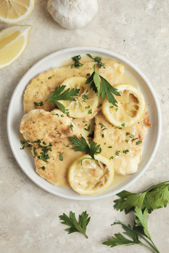 Chicken Francese served on a plate with golden pan-fried chicken breasts in a creamy lemon butter white wine sauce, garnished with fresh herbs and lemon slices.