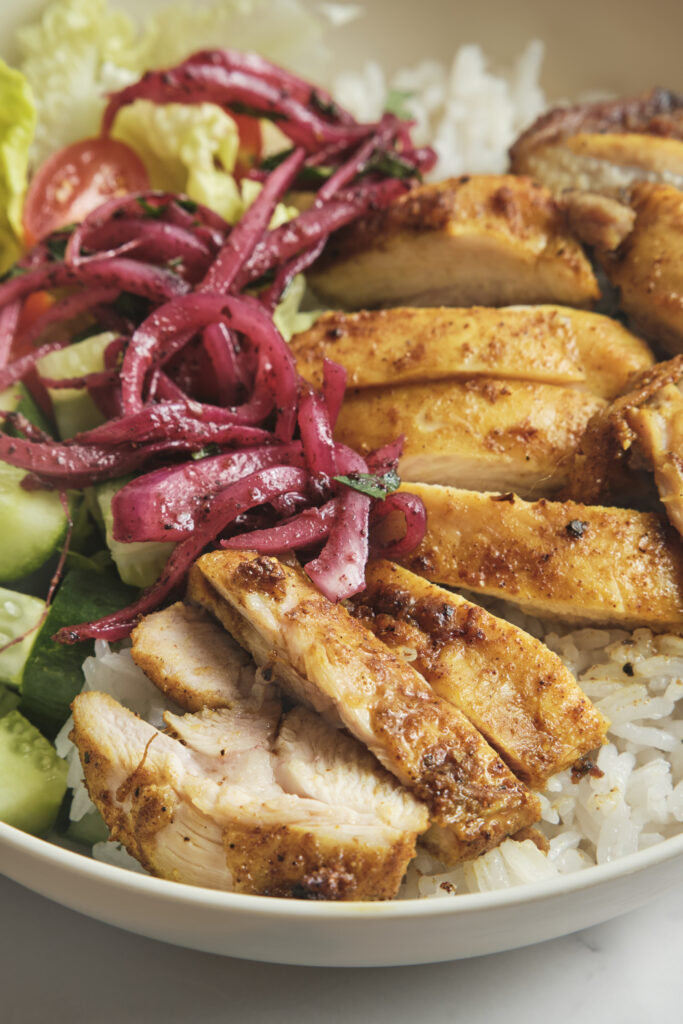 Close-up of chicken shawarma bowl with juicy shawarma chicken, fluffy rice, fresh vegetables, and creamy yogurt garlic sauce—homemade shawarma recipe.