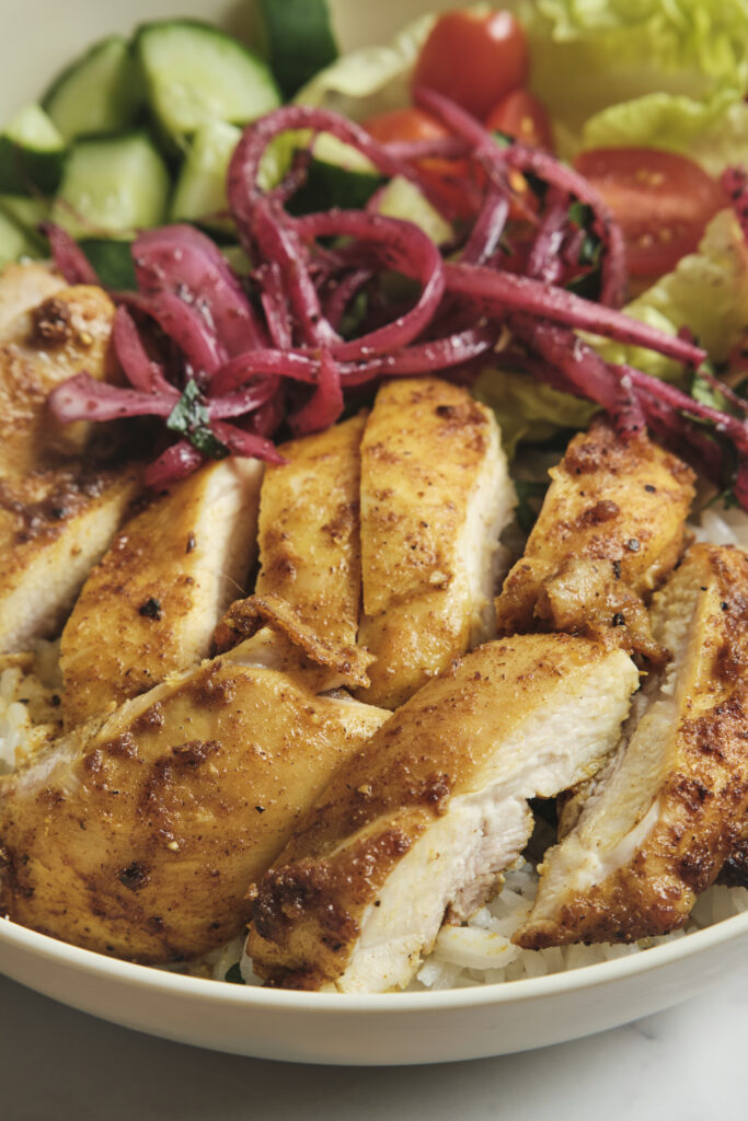 Chicken shawarma bowl with spiced grilled chicken, ginger rice, fresh vegetables, sumac onions, and yogurt garlic sauce—homemade shawarma recipe.