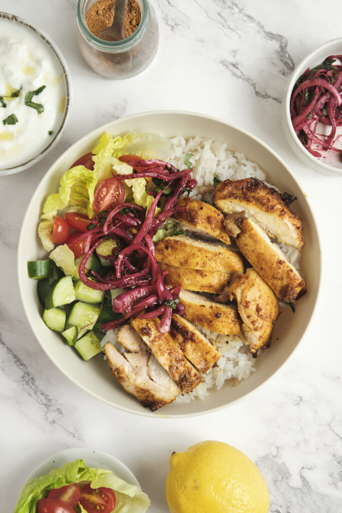 Chicken shawarma bowl with spiced grilled chicken, ginger rice, fresh vegetables, sumac onions, and yogurt garlic sauce—homemade shawarma recipe.
