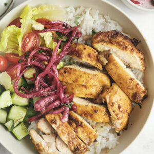 chicken shawarma in a bowl, served with rice, cucumbers, tomatoes and sumac onions.
