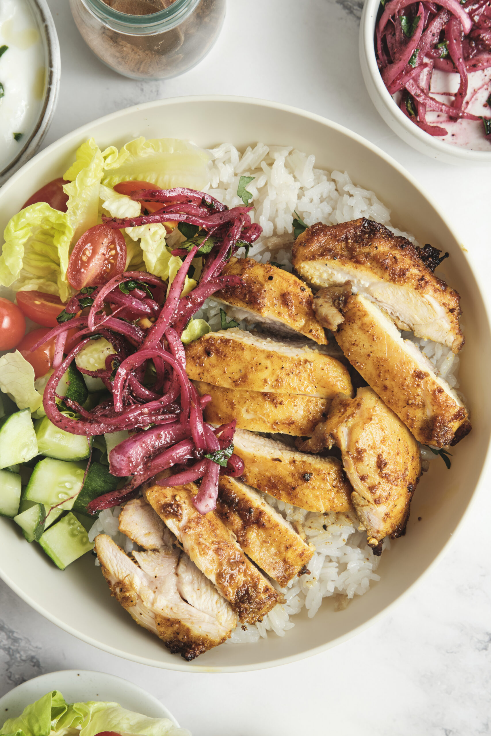 chicken shawarma in a bowl, served with rice, cucumbers, tomatoes and sumac onions.