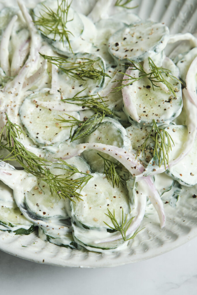 Close-up of crisp English cucumber slices and red onions coated in a creamy yogurt dill dressing for an easy summer salad recipe.