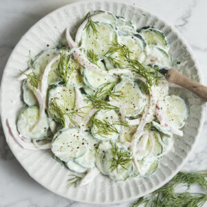 A white bowl filled with creamy cucumber salad with dill and red onions, showcasing a quick 10-minute healthy summer side dish.