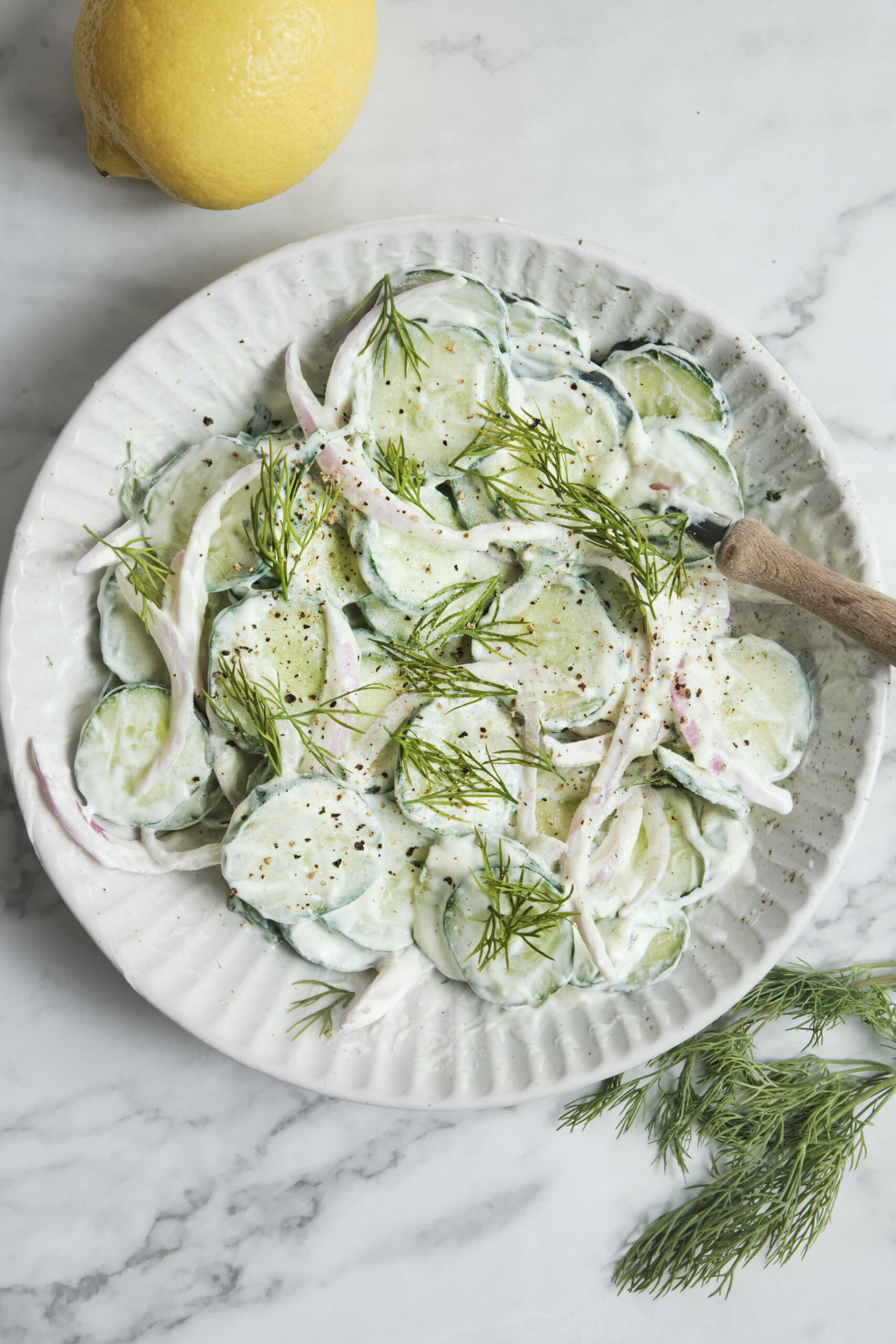 A white bowl filled with creamy cucumber salad with dill and red onions, showcasing a quick 10-minute healthy summer side dish.