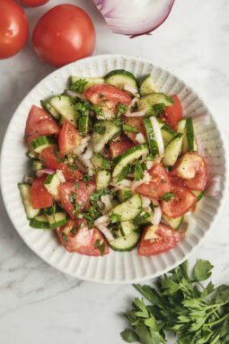 Cucumber, tomato, and onion salad served on a white plate, fresh healthy Mediterranean-style vegetable salad with simple vinaigrette, light and colorful summer dish.
