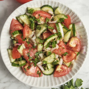 Cucumber, tomato, and onion salad served on a white plate, fresh healthy Mediterranean-style vegetable salad with simple vinaigrette, light and colorful summer dish.