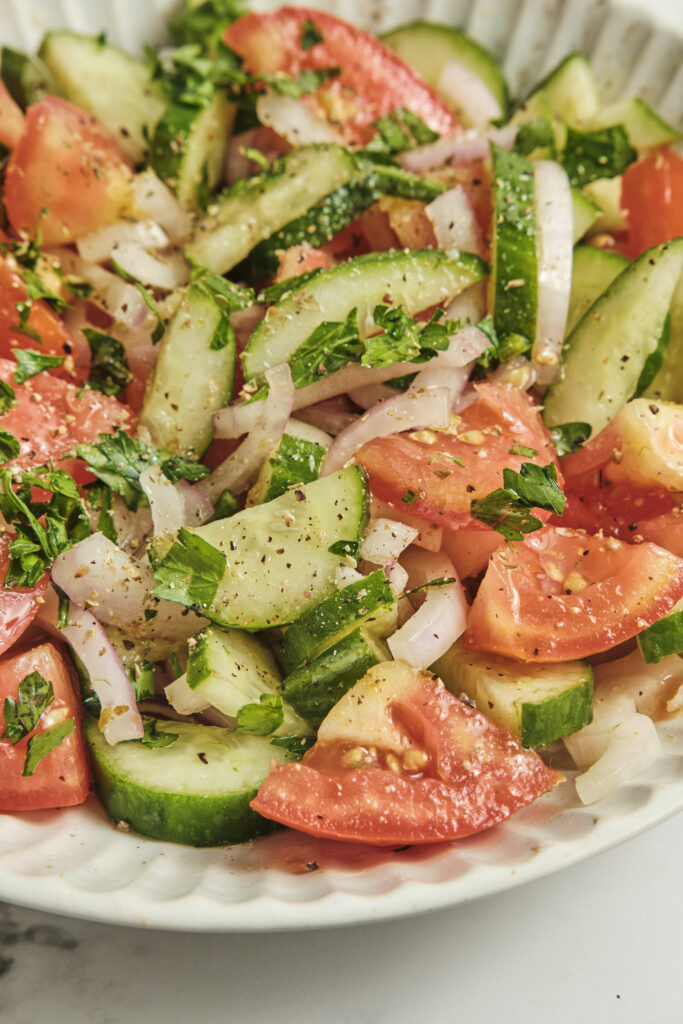 Cucumber, tomato, and onion salad served on a white plate, fresh healthy Mediterranean-style vegetable salad with simple vinaigrette, light and colorful summer dish.