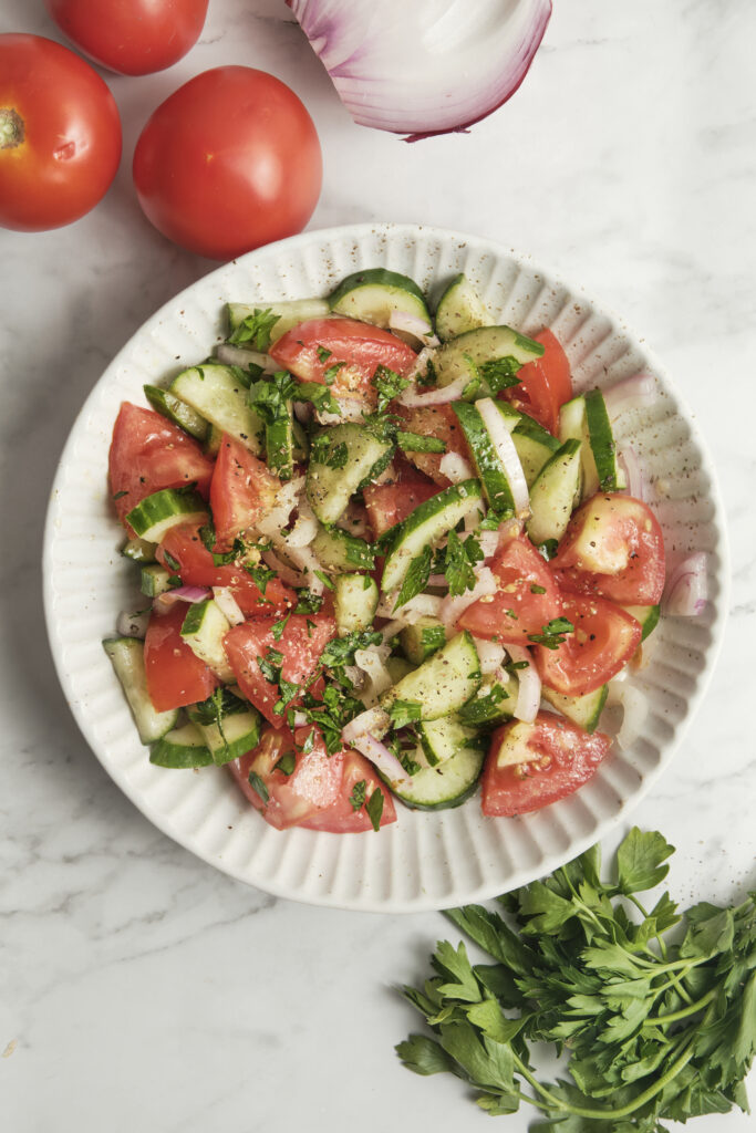 Cucumber, tomato, and onion salad served on a white plate, fresh healthy Mediterranean-style vegetable salad with simple vinaigrette, light and colorful summer dish.