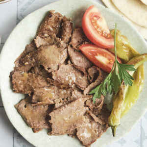 Doner kebab meat served on a plate with roasted vegetables and soft lavash bread, a homemade Turkish-style meal.