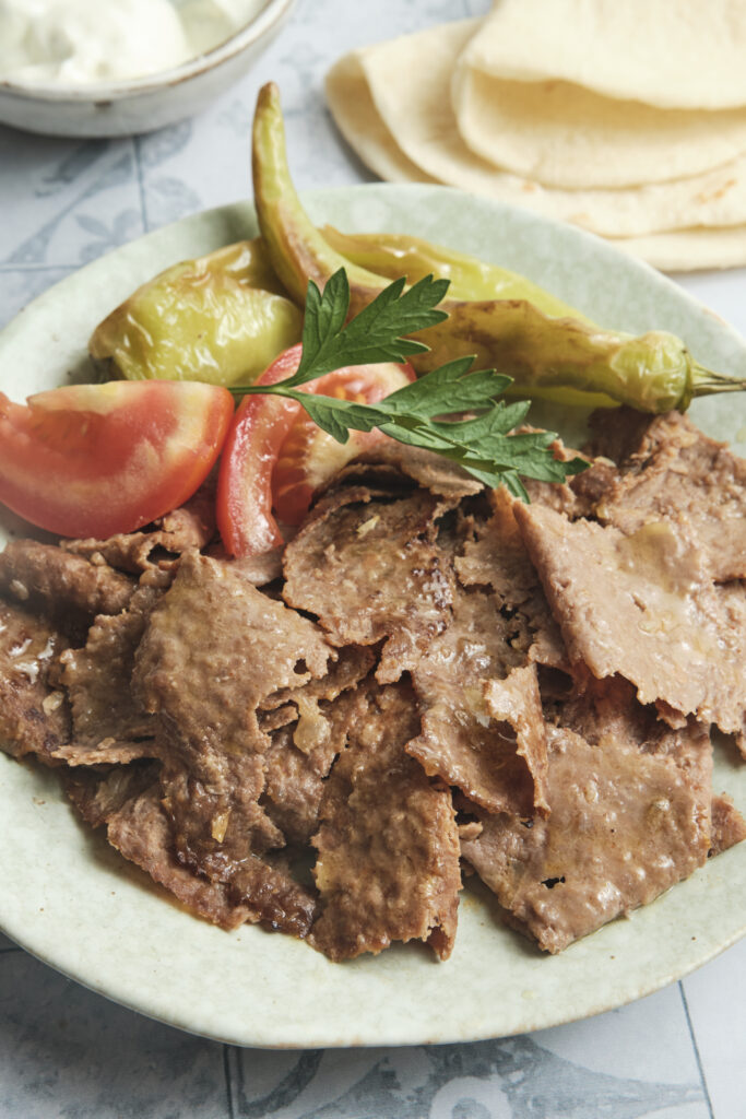 Doner kebab meat served on a plate with roasted vegetables and soft lavash bread, a homemade Turkish-style meal.