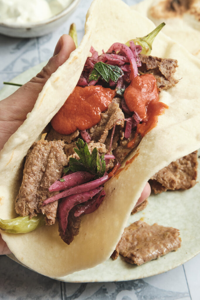 Lavash wrap filled with doner kebab or shawarma meat, fresh salad, and creamy sauce, served as a homemade street food-style flatbread sandwich.
