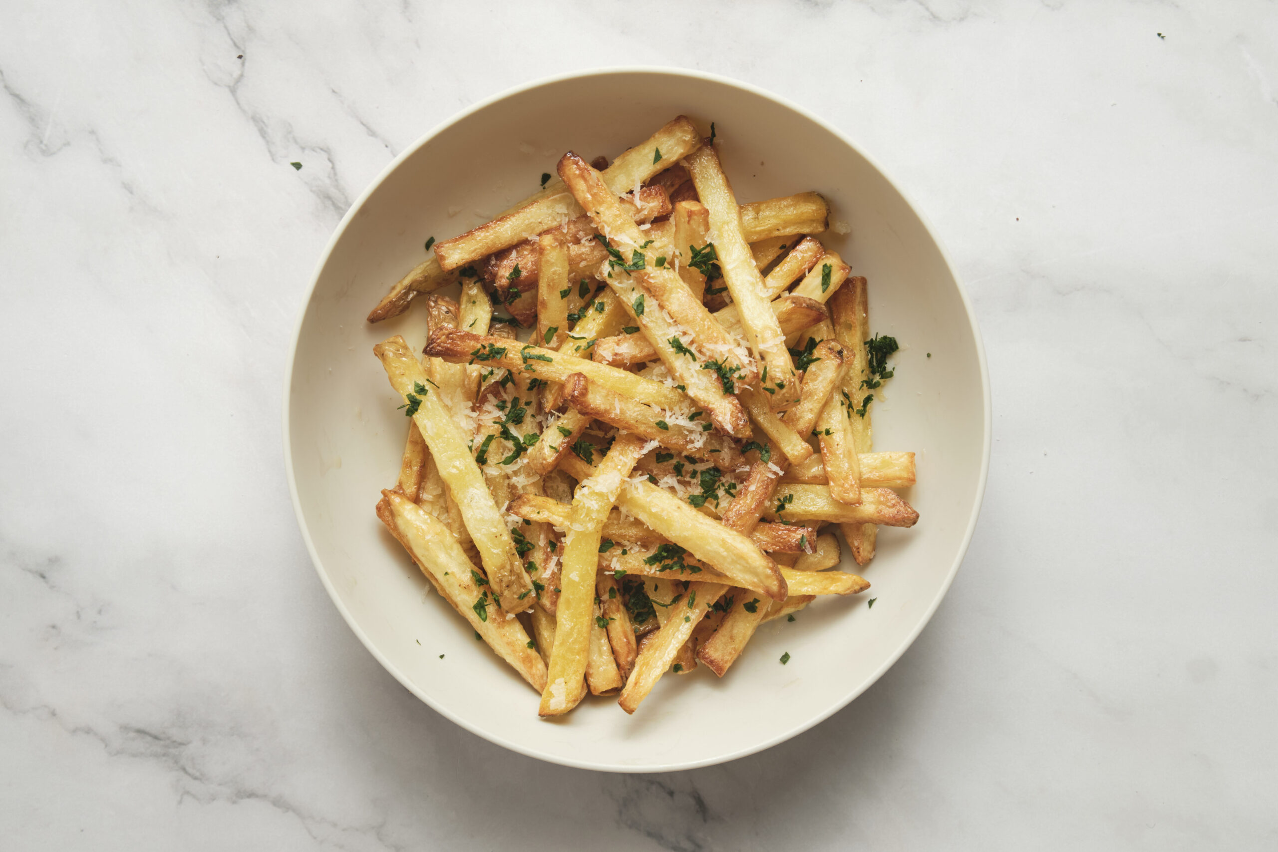 Crispy garlic parmesan french fries in a bowl, made in the air fryer and topped with grated parmesan cheese and herbs, perfect as an easy side dish or snack.