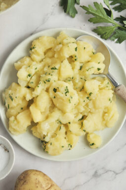 Close-up of German potato salad served in a rustic bowl with sliced potatoes, fresh herbs, red onion, and a light tangy dressing, garnished with parsley and black pepper.