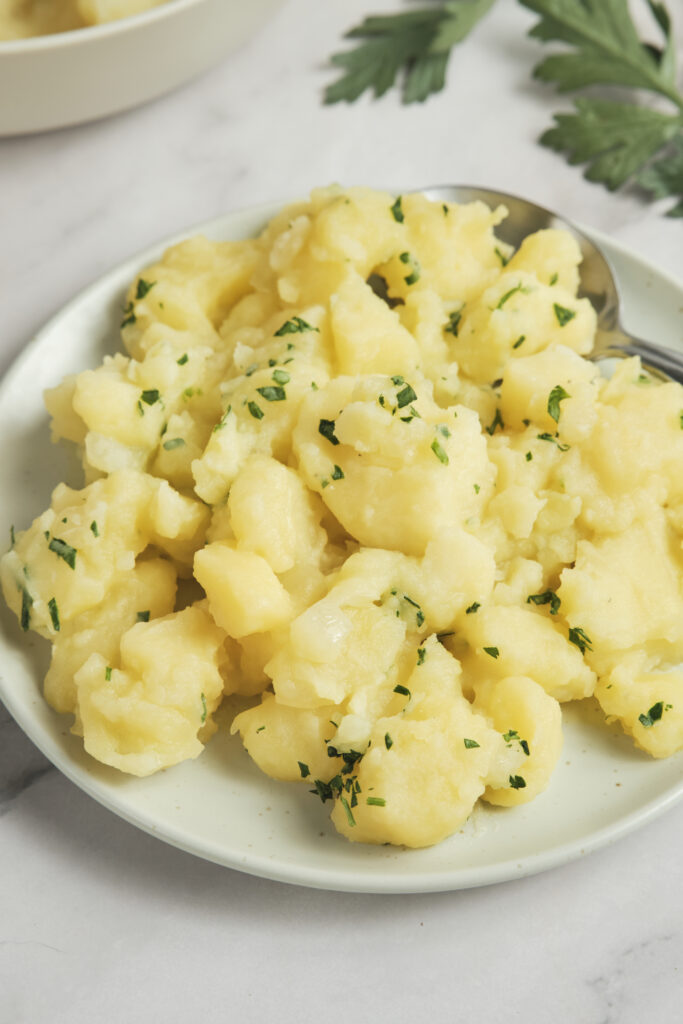Close-up of German potato salad served in a rustic bowl with sliced potatoes, fresh herbs, red onion, and a light tangy dressing, garnished with parsley and black pepper.