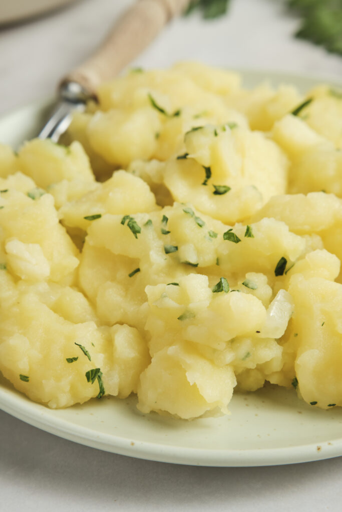 Close-up of German potato salad served in a rustic bowl with sliced potatoes, fresh herbs, red onion, and a light tangy dressing, garnished with parsley and black pepper.