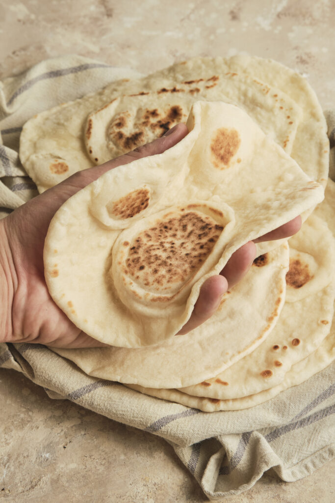 Fresh homemade lavash bread held in hands, showing the soft, thin, and flexible texture of the traditional flatbread.