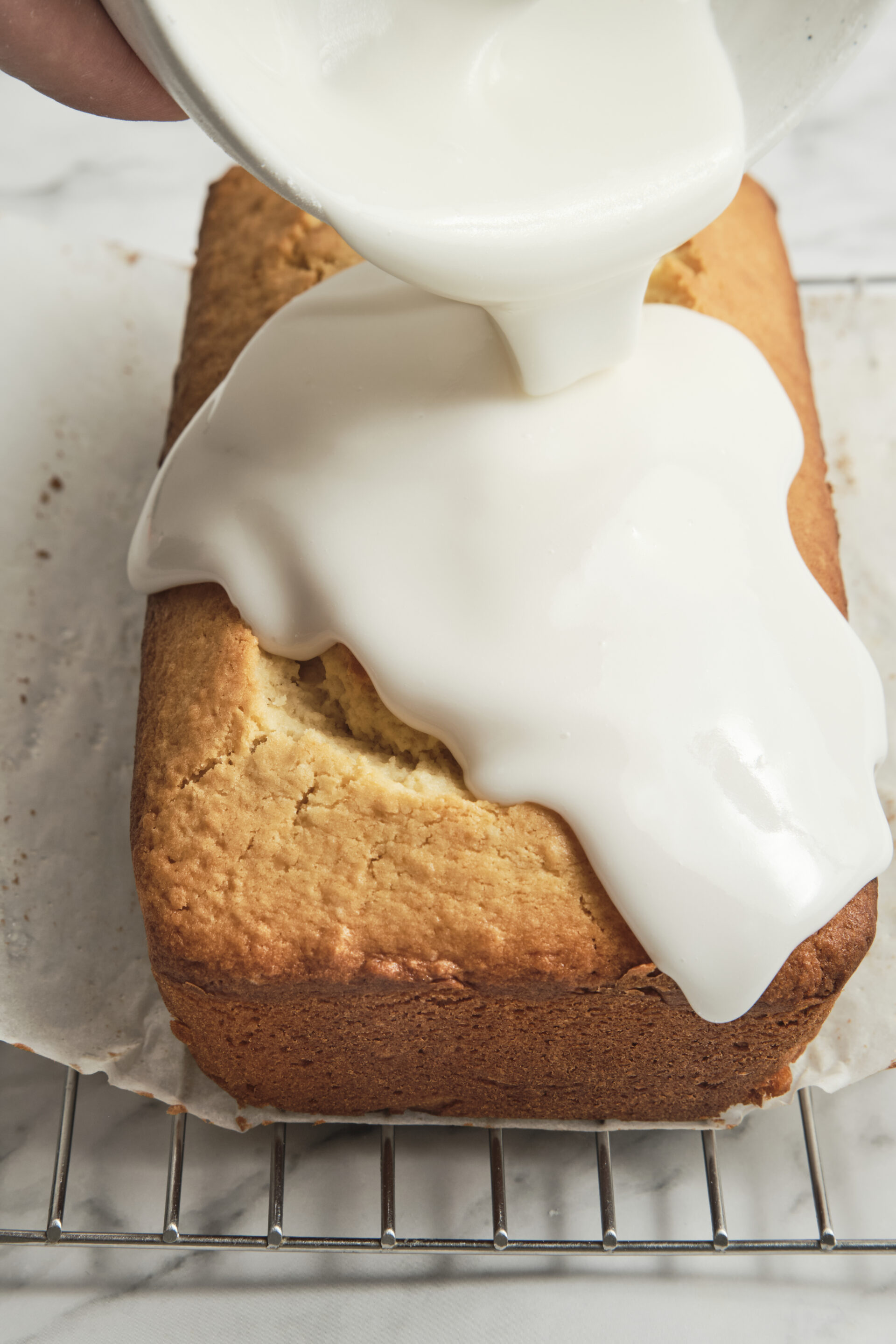 Easy homemade lemon glaze being poured over a freshly baked cake, creating a glossy citrus icing that drips down the sides.