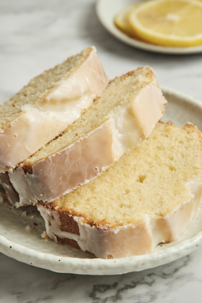 Slices of moist lemon loaf cake served on a plate with glossy lemon glaze drizzled over the top, garnished with fresh lemon slices for a bright homemade dessert.
