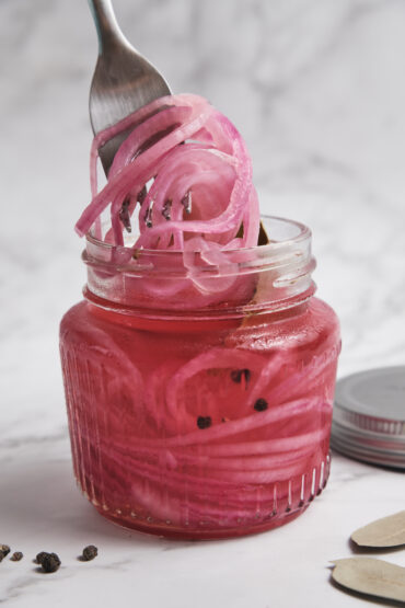 Quick pickled red onions being lifted from a glass jar with a fork, showing their vibrant pink color and crisp texture in natural light.