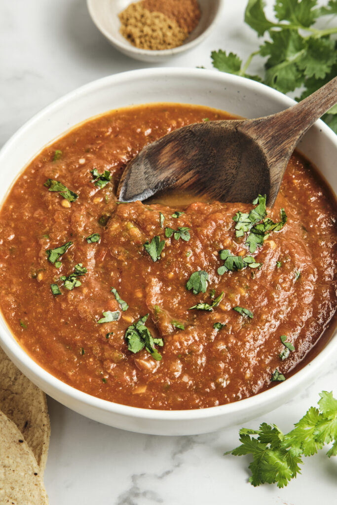Bowl of authentic ranchero sauce made with roasted tomatoes, jalapeños, onion, garlic, and fresh cilantro, featuring a rich smoky texture and vibrant red color.