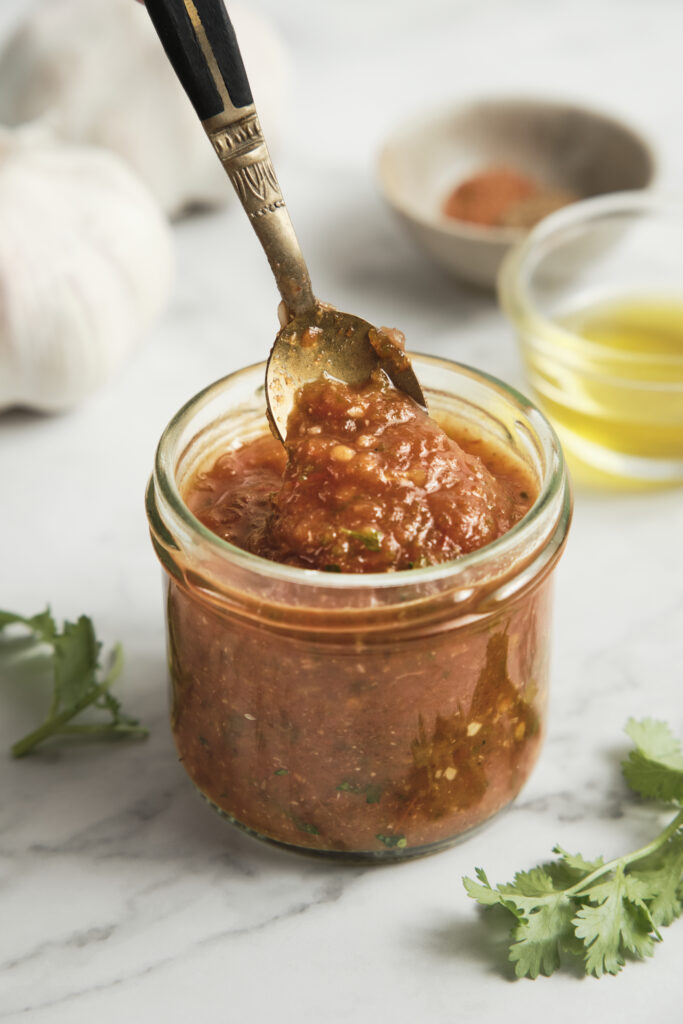 Jar of authentic ranchero sauce made with roasted tomatoes, jalapeños, onion, garlic, and fresh cilantro, featuring a rich smoky texture and vibrant red color.