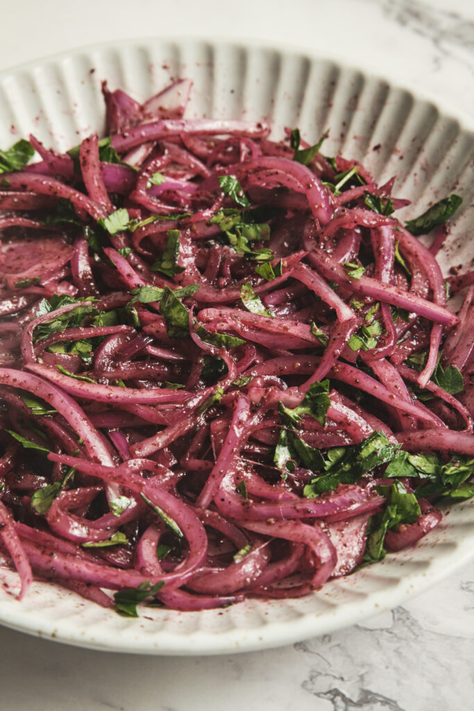 Fresh sumac onions made with thinly sliced red onions and sumac in a bowl—easy Middle Eastern red onion salad recipe.