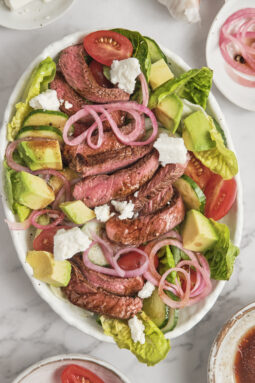 Juicy grilled steak served over fresh greens with avocado, cherry tomatoes, red onions, and creamy balsamic dressing in a healthy high-protein steak salad.