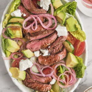 Juicy grilled steak served over fresh greens with avocado, cherry tomatoes, red onions, and creamy balsamic dressing in a healthy high-protein steak salad.