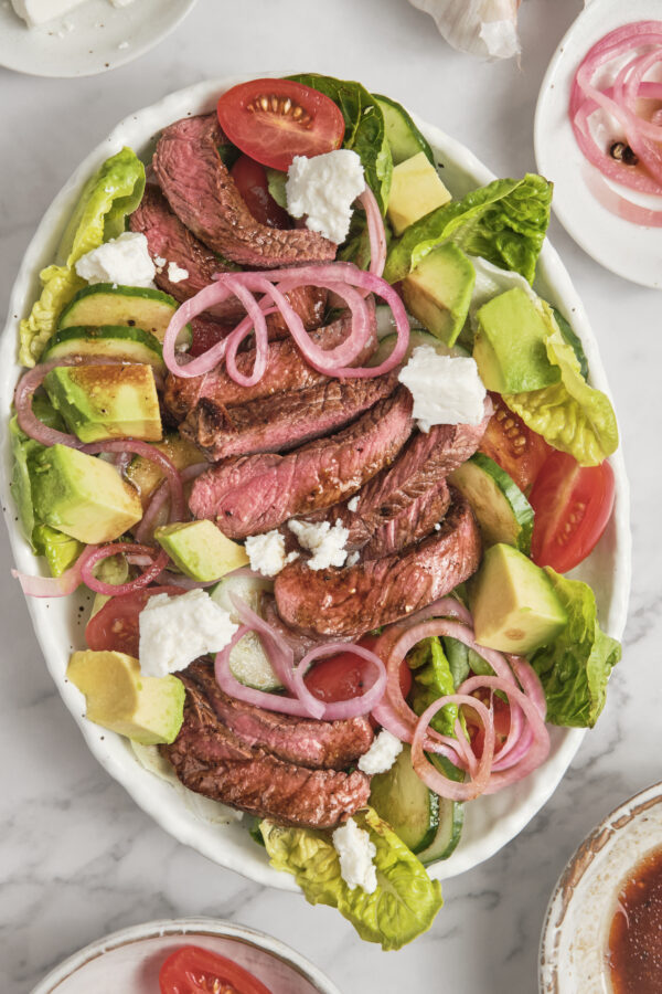 Juicy grilled steak served over fresh greens with avocado, cherry tomatoes, red onions, and creamy balsamic dressing in a healthy high-protein steak salad.