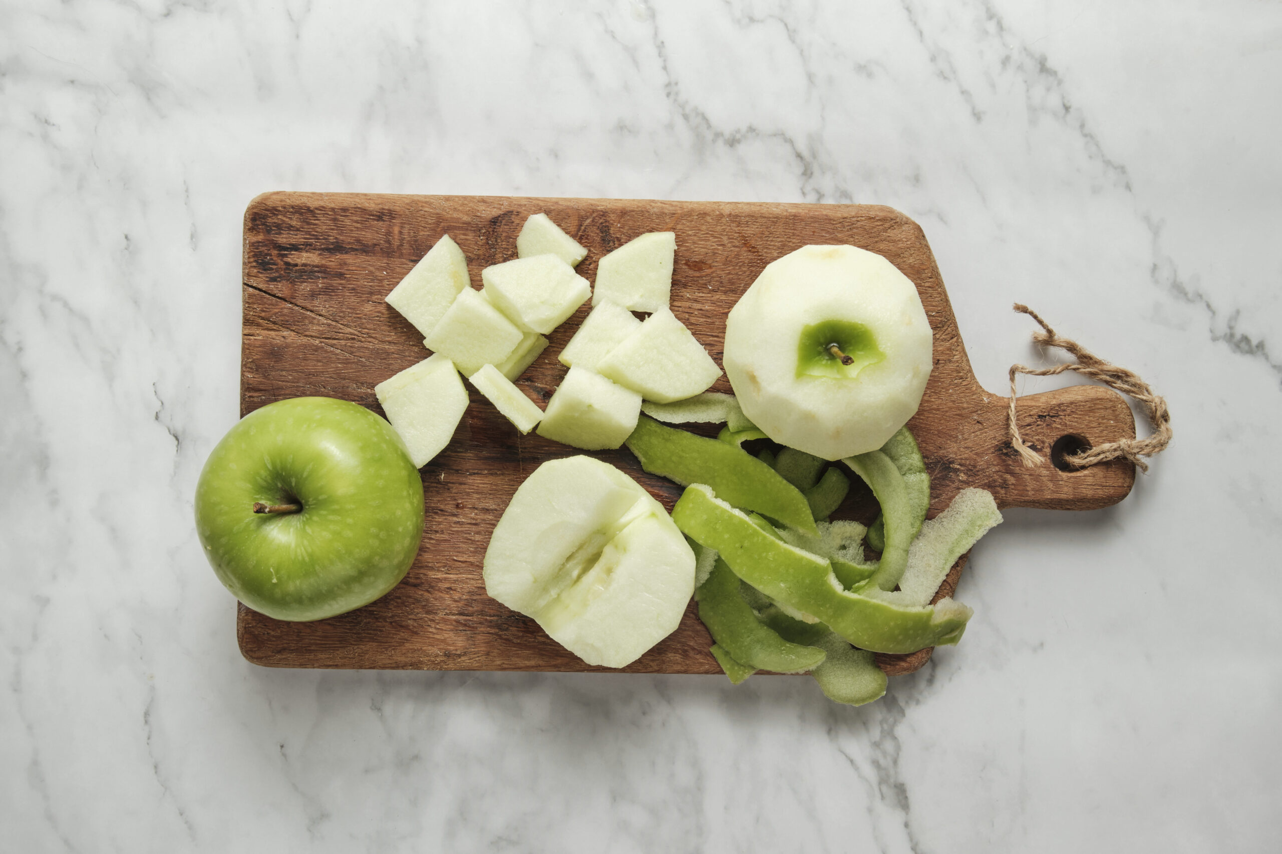 A close-up, top-down view of fresh, green Granny Smith apples being prepared on a light wooden cutting board.