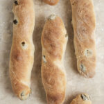 A close-up shot of an olive baguettes packed with chopped green olives and a perfectly golden, crispy crust.
